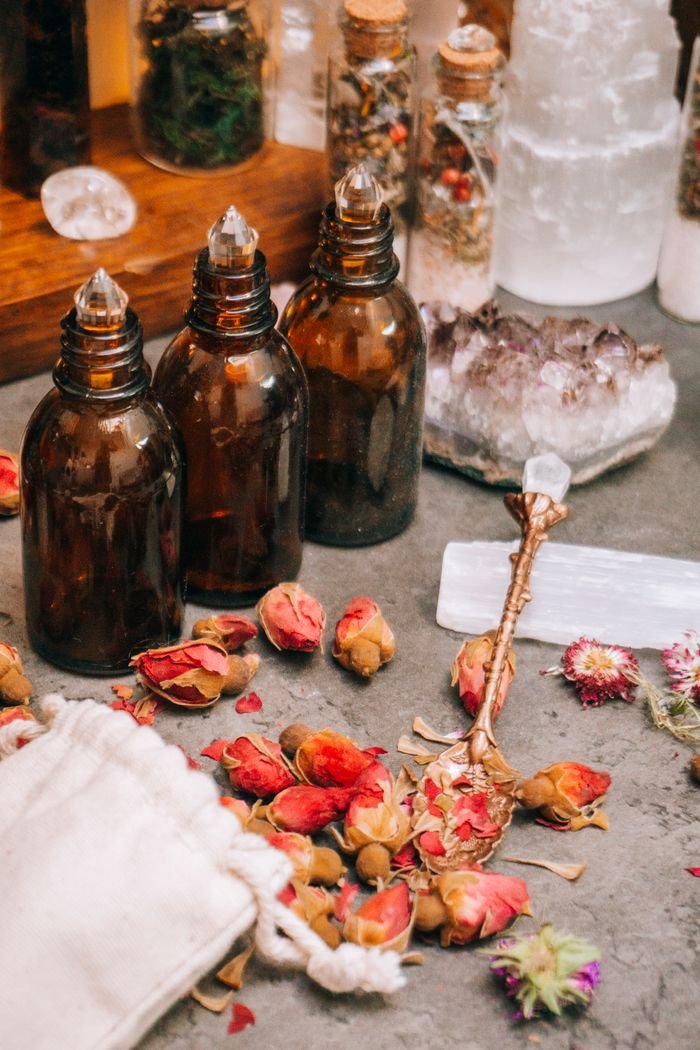 Aesthetic arrangement of brown bottles, dried rose petals, and crystals for aromatherapy.