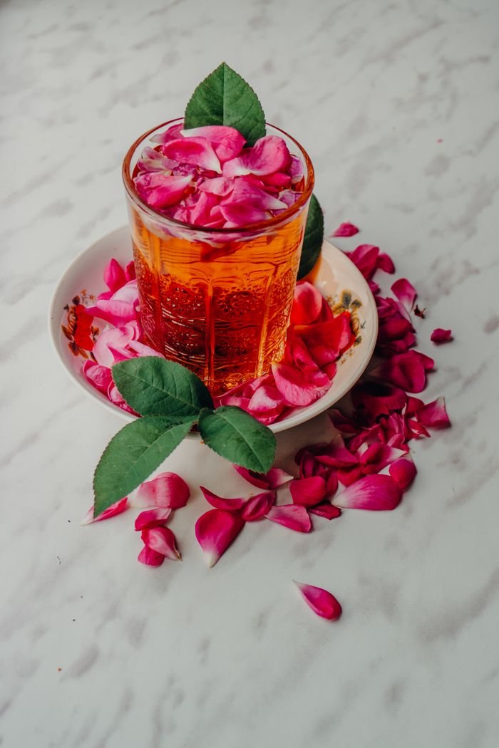 A visually stunning glass of orange beverage surrounded by vibrant rose petals on a marble surface, creating a luxurious ambiance.